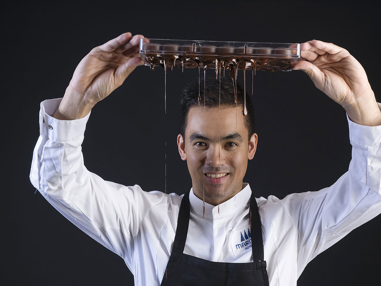 Taro Bünemann, Chef Pâtissier der Orangerie im Maritim Timmendorfer Strand, hält ein Tablett, von dem Schokolade tropft.