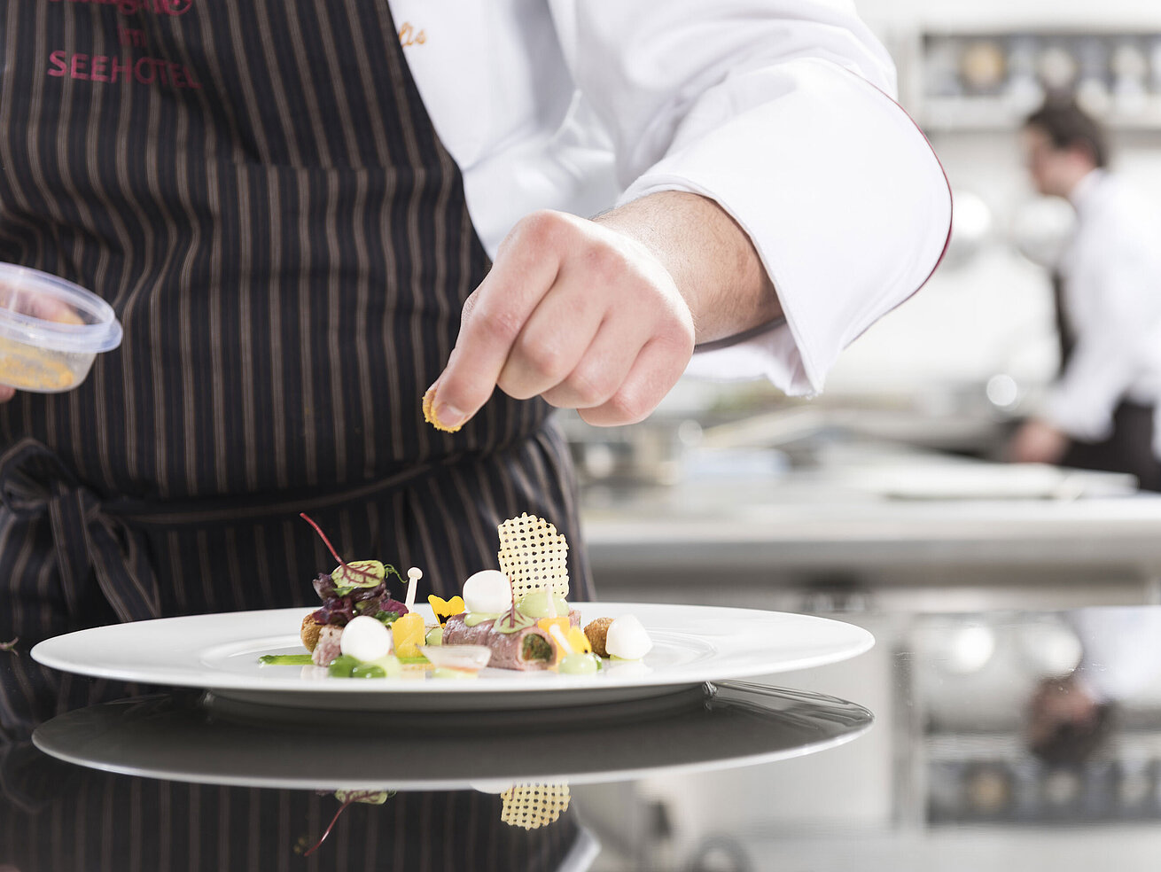 Koch richtet ein Gourmetgericht mit Gemüse, Kräutern und kunstvollen Elementen in der Orangerie an.